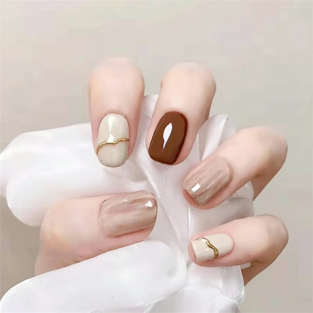 Hand with stylish nail art featuring neutral colors and gold accents.